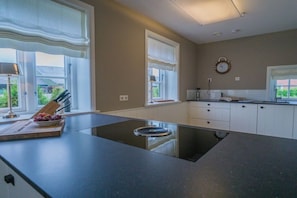 A modern kitchen with a central island, white cabinetry, and large windows. - Holiday home in Goting with swimming pool (Goting)