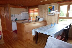 Un interior de madera con cocina, comedor y una ventana con persianas.