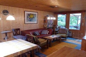 Ein Holzinnenraum mit einem roten Sofa, einem Esstisch und einem Bücherregal.