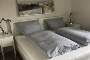 A twin bed with a striped bedspread, two bedside lamps, and a framed picture of a beach scene on the wall. - House on the sea dike (Hedwigenkoog)