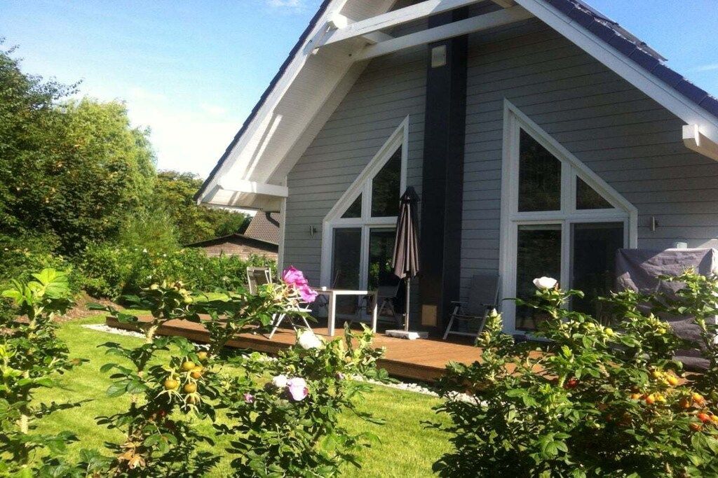 A residential house with a sloped roof, a covered patio, and a garden with various plants and a lawn.