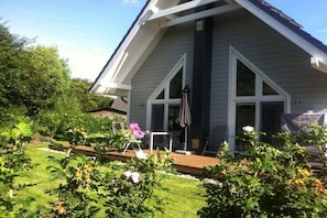 A residential house with a sloped roof, a covered patio, and a garden with various plants and a lawn. - House on the sea dike (Hedwigenkoog)