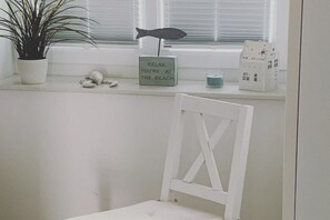A white chair, a potted plant, a fish-shaped ornament, a sign, and a small house model on a window sill. - House on the sea dike (Hedwigenkoog)