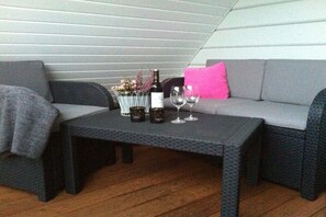 A cozy seating area with a sofa and a small table, a bottle of wine, and a glass on the table. - House on the sea dike (Hedwigenkoog)