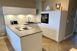 A compact kitchen with a built-in oven, a sink, and a countertop with a coffee maker. - Holiday apartment with 1 bedroom (Lübeck-Travemünde)