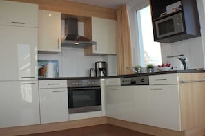 A modern kitchen with white cabinetry, a built-in oven, a coffee maker, and a microwave. - Holiday apartment with 2 bedrooms (Großenbrode)