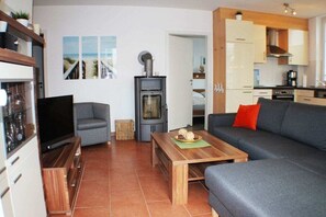 Moderni olohuone, jossa on sohva, televisio, takka ja keittiöalue.