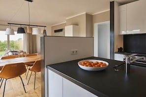 A modern kitchen with a black countertop, a bowl of oranges, and a dining area with orange chairs. - Strandhaus Strandgut new 2017 (Großenbrode)