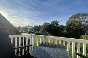 Ein Balkon mit Glastisch und Stühlen, mit Blick auf eine grüne Landschaft und Häuser.
