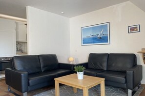 Ein Wohnzimmer mit zwei schwarzen Ledersofas, einem Holztisch, einer Topfpflanze und einem gerahmten Bild von einem Segelboot an der Wand.