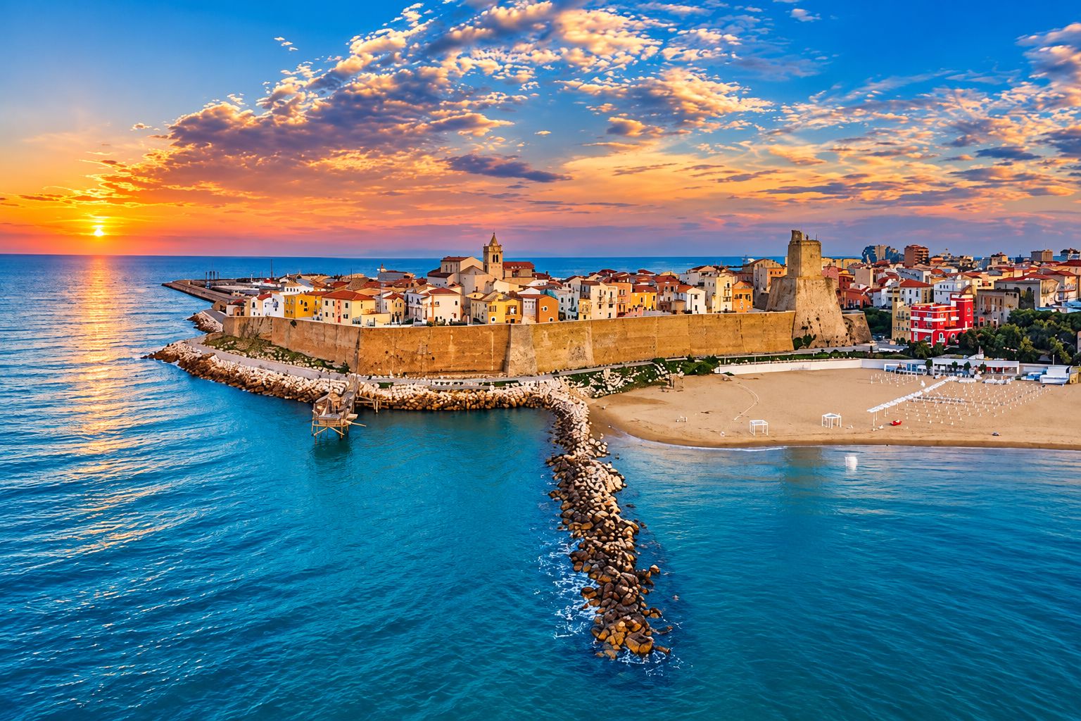 A coastal cityscape with a prominent fortification, a beach, and a sunset.