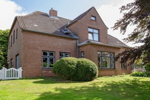 A two-story brick house with a sloped roof, a white picket fence, and a well-maintained lawn. - at the Kahlcke holiday farm 2 (Reinsbüttel)