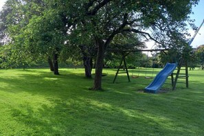 Un parque con un columpio, un tobogán y árboles.