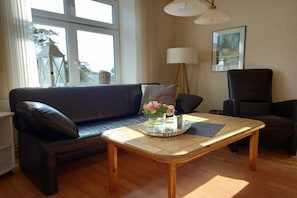 A living room with a dark leather sofa, a wooden coffee table with a tray and flowers, a lamp, and a painting on the wall. - at the Kahlcke holiday farm 2 (Reinsbüttel)