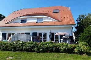 Ein zweistöckiges Haus mit geneigtem Dach, einer überdachten Terrasse und Gartenmöbeln sowie einem gepflegten Garten.