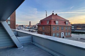 A red brick building with a sloped roof, located near a waterfront with a pedestrian walkway. - Holiday apartment with 1 bedroom (Wismar)