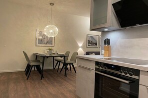 A modern kitchen with a built-in oven, a dining table with chairs, and a pendant light fixture. - Holiday apartment with 1 bedroom (Wismar)