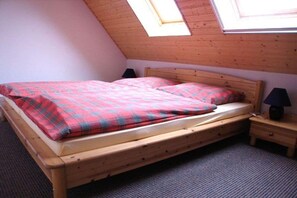 Ein Einzelbett mit Holzrahmen und einer rot-blauen karierten Bettdecke in einem Zimmer mit schrägem Dach und Oberlicht.