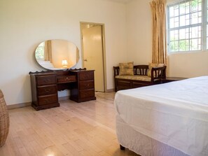 Un dormitorio con cama, cómoda con cajones, silla, espejo y ventana con cortinas.