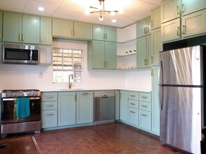 Una cocina con gabinetes verde claro, electrodomésticos de acero inoxidable y suelo de madera.