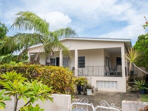 A two-story building with a balcony, surrounded by tropical plants. - Mango Overboard Garden Retreat in the Heart of the South Coast (Bridgetown)