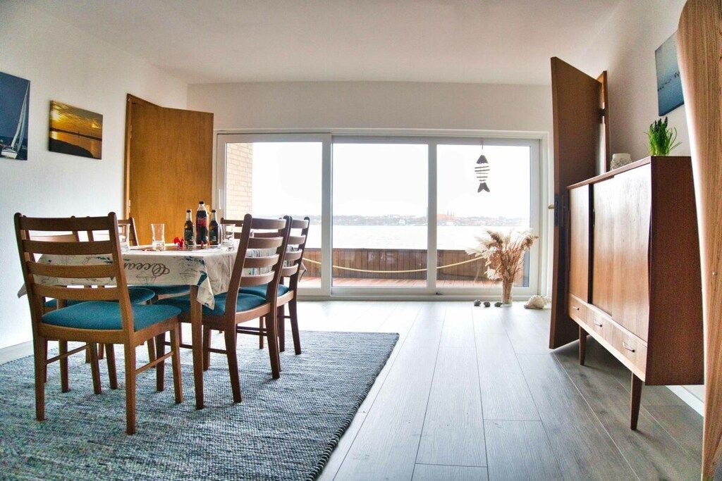 Ein Essbereich mit Tisch für vier Personen, einer Couch und Meerblick durch große Fenster.