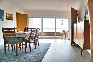Ein Essbereich mit Tisch für vier Personen, einer Couch und Meerblick durch große Fenster.