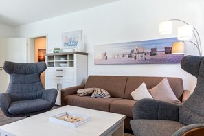 Ein Wohnzimmer mit einer Couch, zwei Sesseln, einem Couchtisch und einem Gemälde an der Wand.
