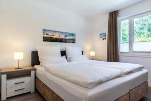 Ein ordentlich bezogenes Bett mit weißen Leinentüchern, ein Nachttisch mit Lampe und ein Gemälde an der Wand.
