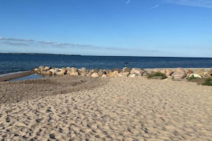 Ein Sandstrand mit einem steinernen Wellenbrecher und ruhiger See.