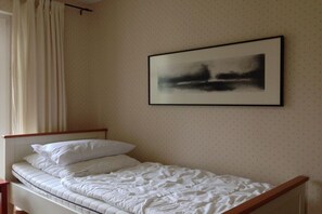 A single bed with white bedding in a room with a plain wall and a framed abstract painting. - Holiday apartment with 2 bedrooms (Graal Müritz)