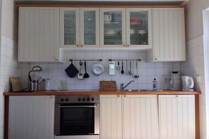 Ett kök med vita skåp, en inbyggd ugn och diverse köksredskap som hänger på väggen.