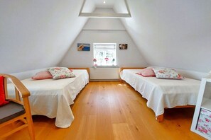 A room with two single beds, a wooden floor, a sloped ceiling, and a window with a view. - Holiday home with 2 bedrooms (Brodersby-Goltoft)