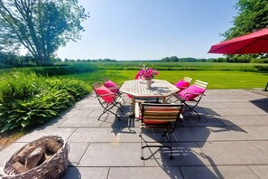 An outdoor patio with a round table and chairs, surrounded by greenery and a clear sky. - Holiday home with 2 bedrooms (Brodersby-Goltoft)