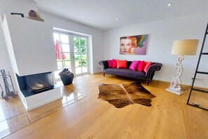 A modern living room with a fireplace, a sofa with red cushions, a cowhide rug, and a painting on the wall. - Holiday home with 2 bedrooms (Brodersby-Goltoft)