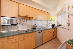 A compact kitchen with wooden cabinets, a built-in microwave, a dishwasher, and a window with a view of yellow flowers. - ""La Gaviota"" in Villa Gudrun (Binz)