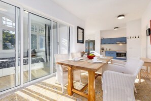 A modern kitchen with blue cabinets, a dining area with a wooden table and white chairs, and a sliding glass door leading to a balcony. - “Meerweib” in Villa Sirene (Ostseebad Binz)