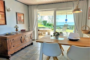 A dining area with a wooden table, white chairs, a cabinet, and a view of the outdoors. - Beach house "Klein Westerland" (Brodersby)