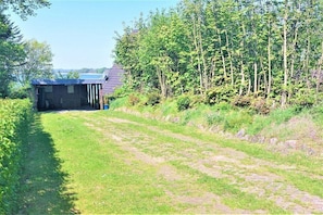 A rural property with a covered structure, a grassy path, and dense trees. - Beach house "Klein Westerland" (Brodersby)