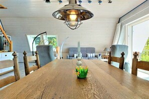 A dining area with a wooden table, chairs, a hanging light fixture, and a window providing natural light. - Beach house "Klein Westerland" (Brodersby)