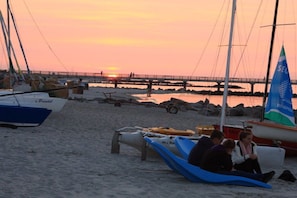 A beach scene with boats, a bridge, and a sunset. - Holiday home with 3 bedrooms (Schönberg)