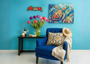 Un sillón azul con un plaid estampado, un jarrón con tulipanes, una botella de vino y copas sobre una mesita auxiliar negra.