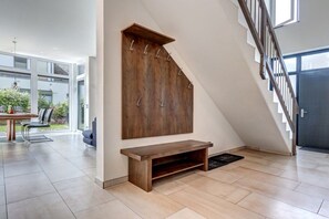 Un intérieur moderne avec un banc en bois, un escalier et un coin repas comprenant des chaises et une table.