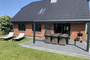 Ein Haus mit überdachter Terrasse, Gartenmöbeln und einem Grill.