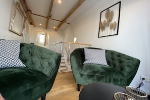 Ein Zimmer mit zwei grünen Samsofas, einer Treppe und einem gerahmten Kunstwerk an der Wand.