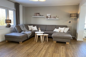Ein modernes Wohnzimmer mit einem grauen Ecksofa, zwei kleinen runden Tischen und einer Stehlampe.