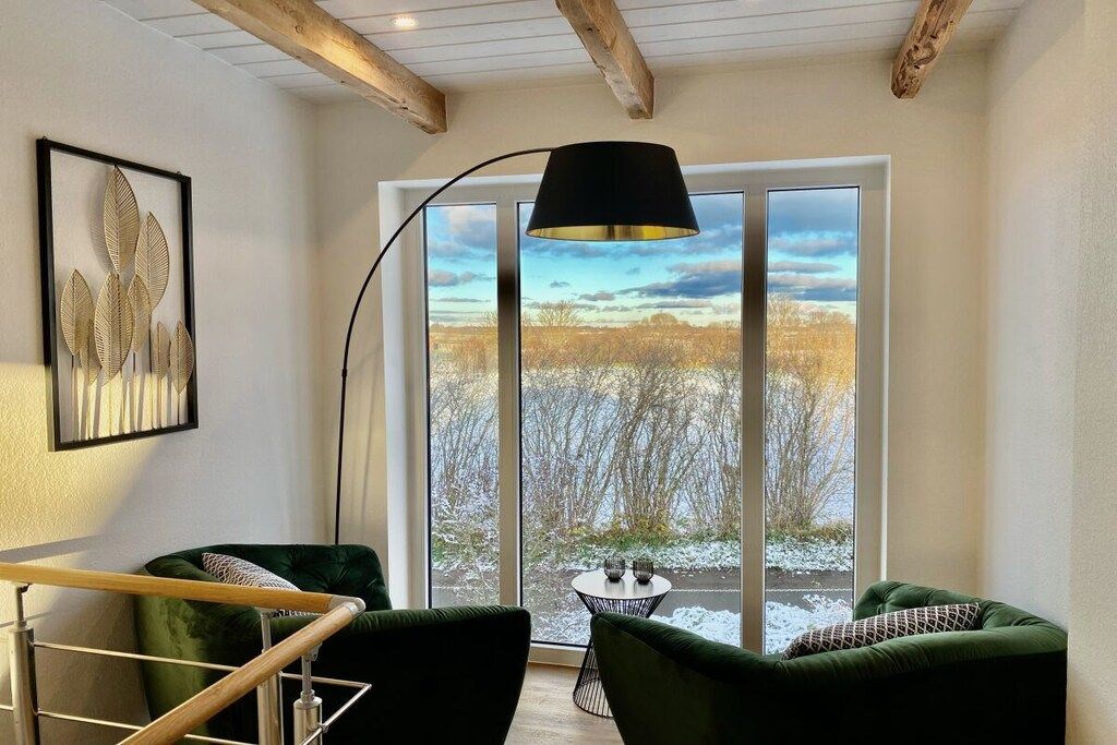 Une pièce avec une grande fenêtre, un canapé vert, une petite table ronde et une lampe.