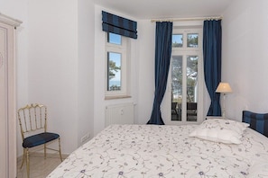 A bedroom with a bed, a chair, a window with curtains, and a lamp. - Baltic Melody with panoramic Baltic Sea views (Ostseebad Binz)
