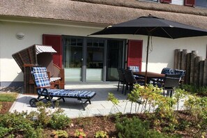 Eine Terrasse im Freien mit Tisch und Stühlen, einer Liege und einem großen Sonnenschirm.