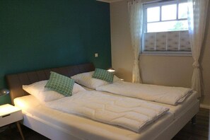 Ein Doppelzimmer mit zwei Betten, einem Nachttisch, einem Fenster mit Vorhängen und einer teal-farbenen Wand.